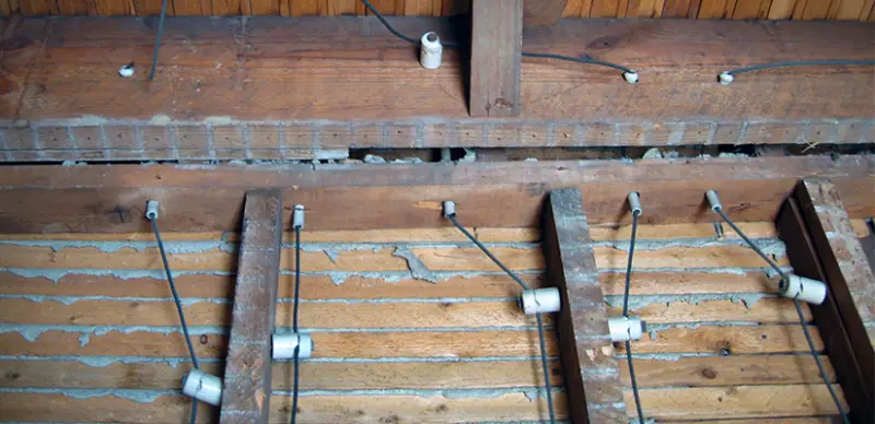 An example of knob and tube wiring: White ceramic knobs attached to joists and white ceramic tubes through joists, with wires running through knobs and tubes