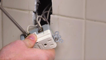 Person attaching wires to a GFCI outlet on a white tiled wall.